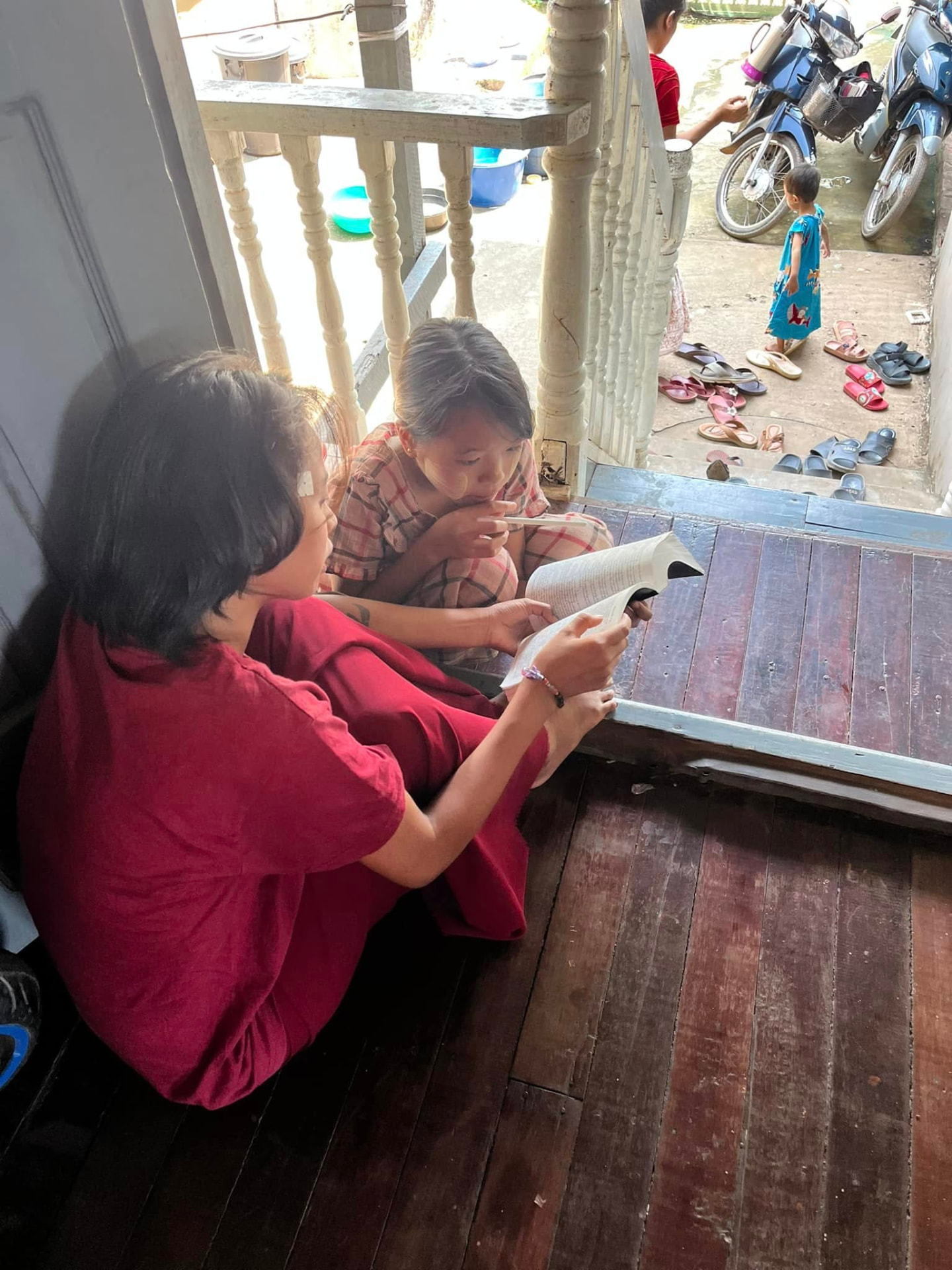 Two young girls reading the Bible together in a doorway in Burma
